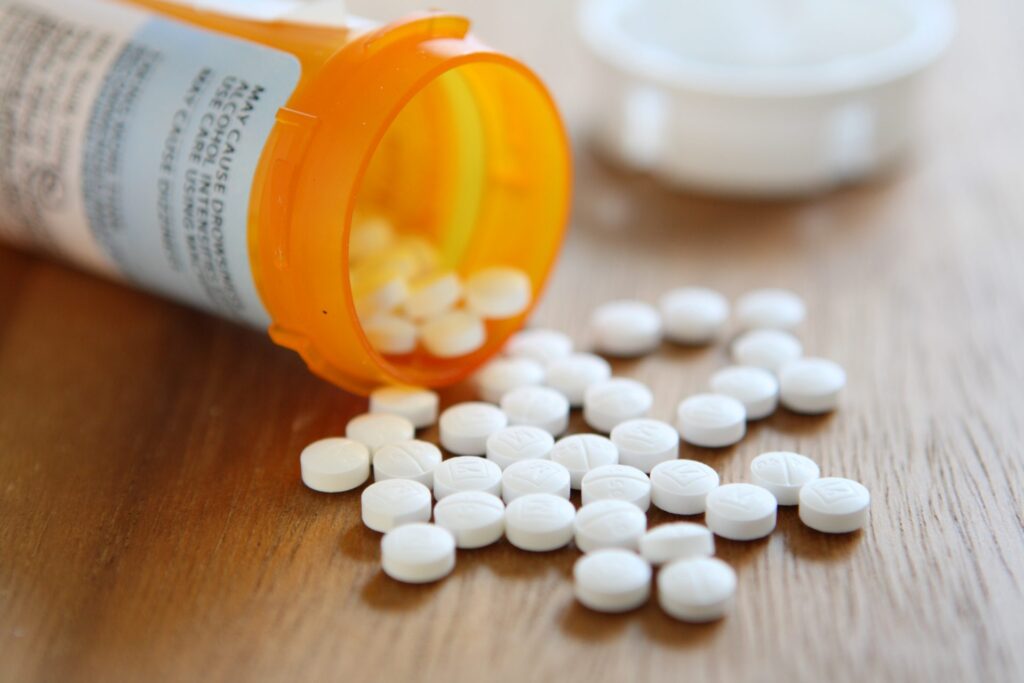 An orange bottle of prescription drugs spilling white pills, representing how one can benefit from calling a Portland criminal defense attorney.