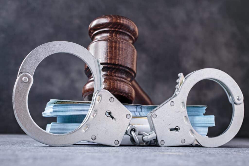 A wooden gavel on top of a pile of cash behind a set of handcuffs, representing how one can benefit from calling a Portland criminal defense attorney.