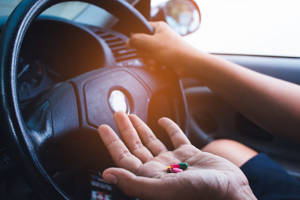 A person driving with pills on their hand, representing how one can benefit from calling a Portland criminal defense attorney.