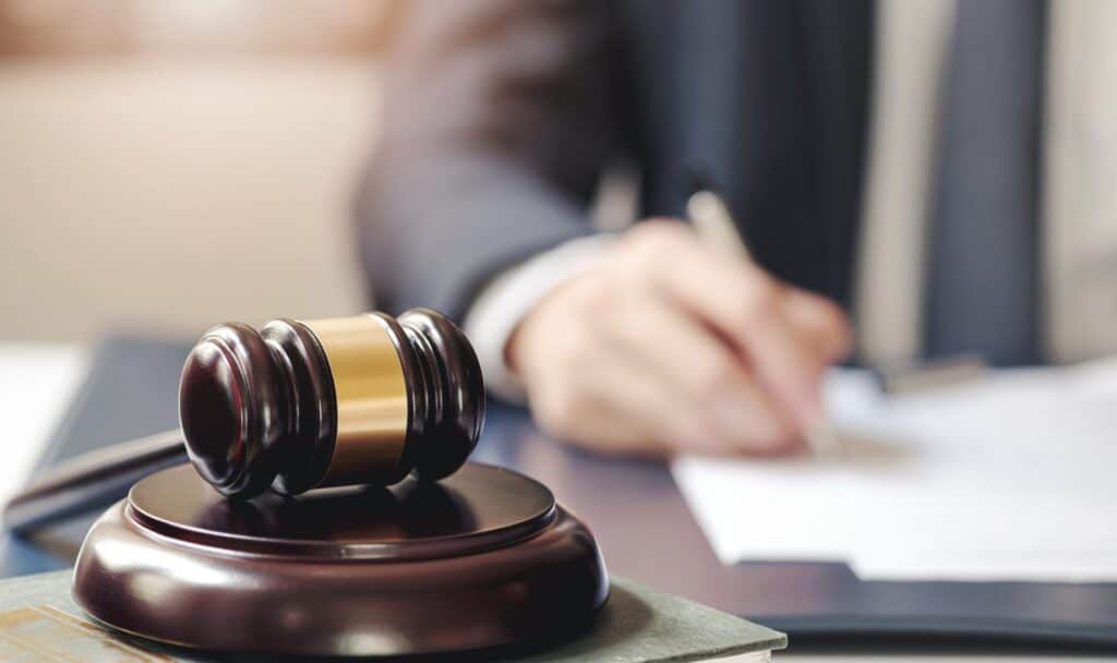 A lawyer writing on some paperwork in front of him there is a gavel on block, representing how one can benefit from calling a Portland criminal defense attorney.