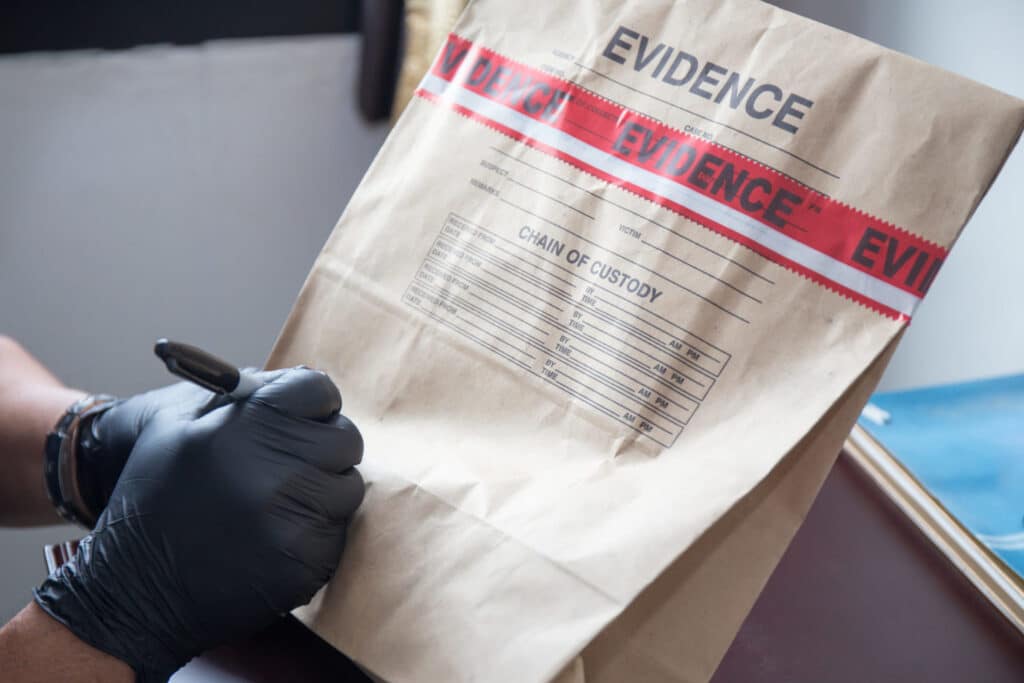 A man wearing dark gloves writing in an envelope label "Evidence", representing how one can benefit from calling a Portland criminal defense attorney.
