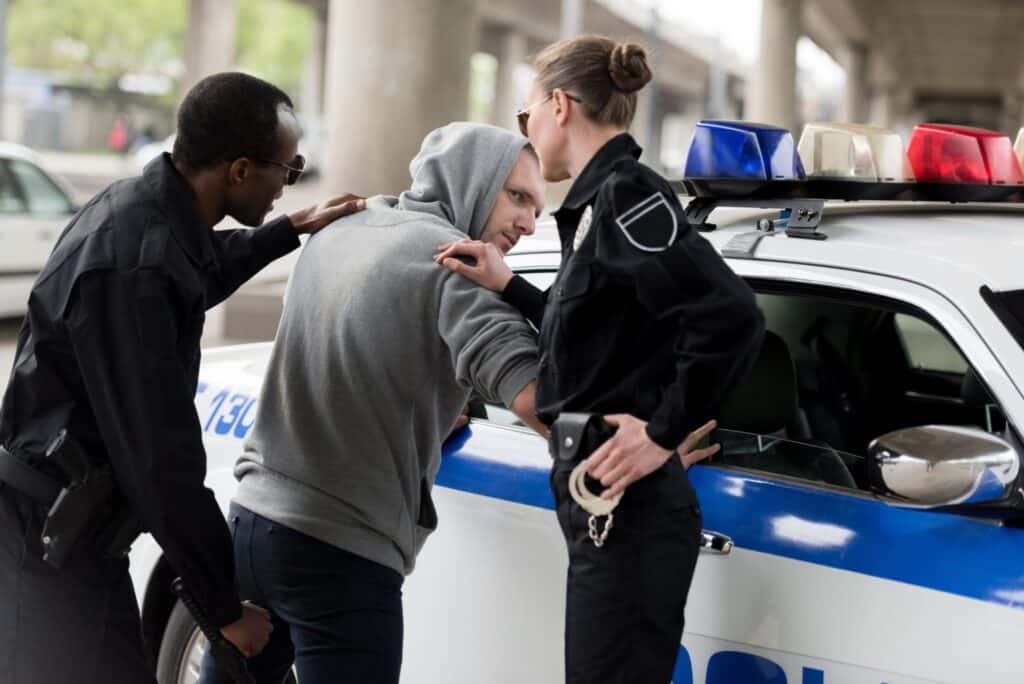 A man getting arrested by a male and a female officer, representing how one can benefit from calling a Portland criminal defense lawyer.