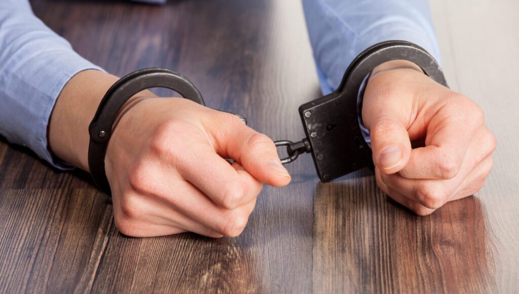 A man wearing handcuff with his hands on a table, representing how one cane benefit from calling a Maine criminal defense lawyer.