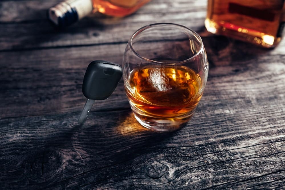 2nd OUI Charges in Maine State portrayed by a car key against a whiskey glass sitting on a pub table.